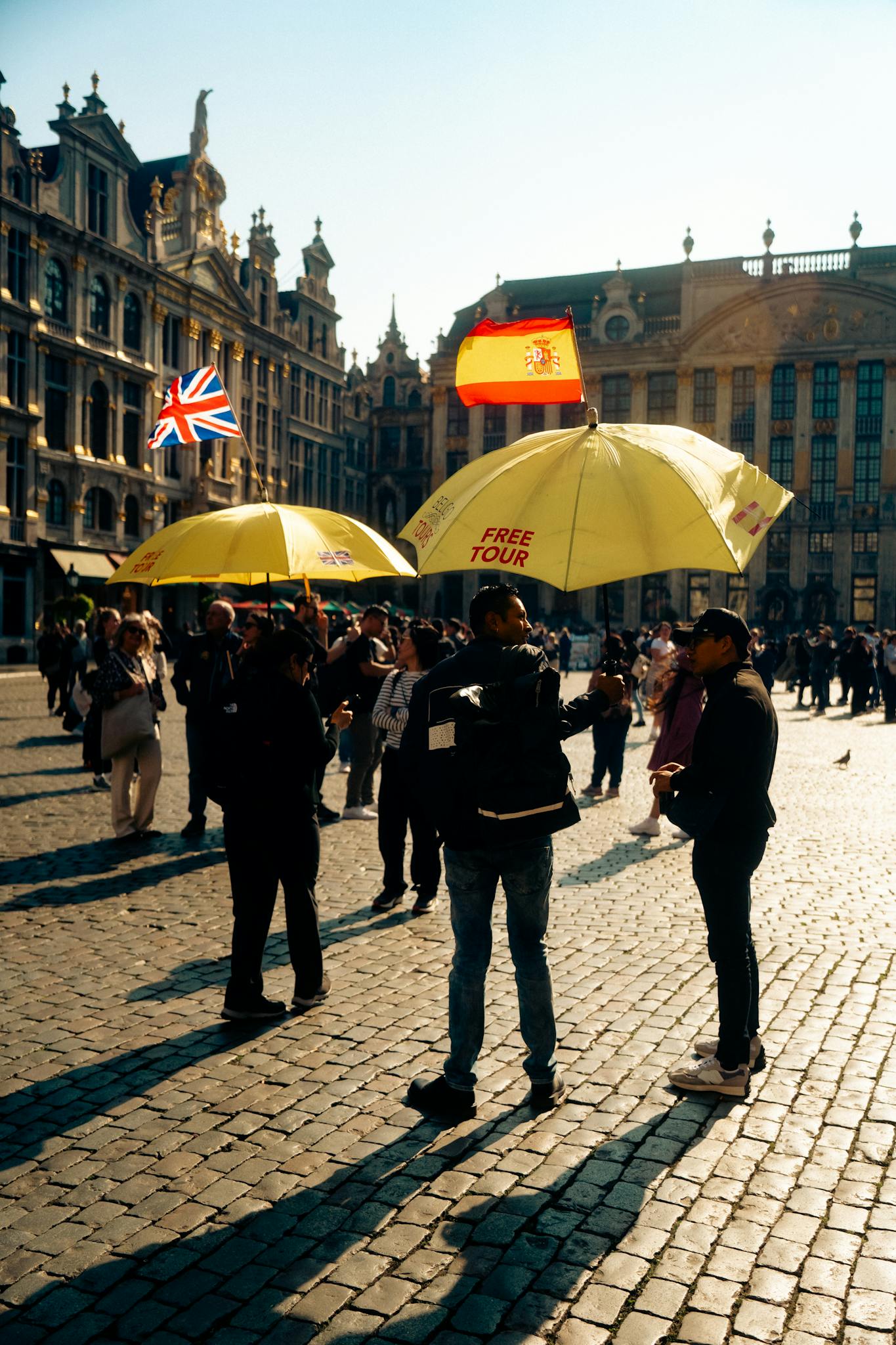 Tourists gather under yellow umbrellas for a free tour at Brussels' historic square.